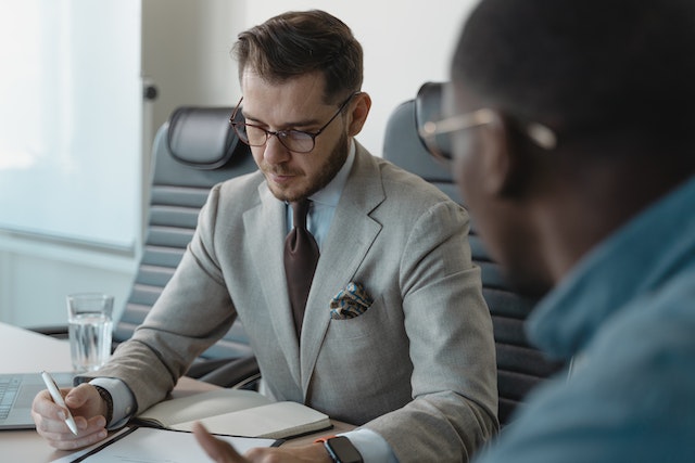 Person in a grey suit interviewing someone in a blue shirt while taking notes